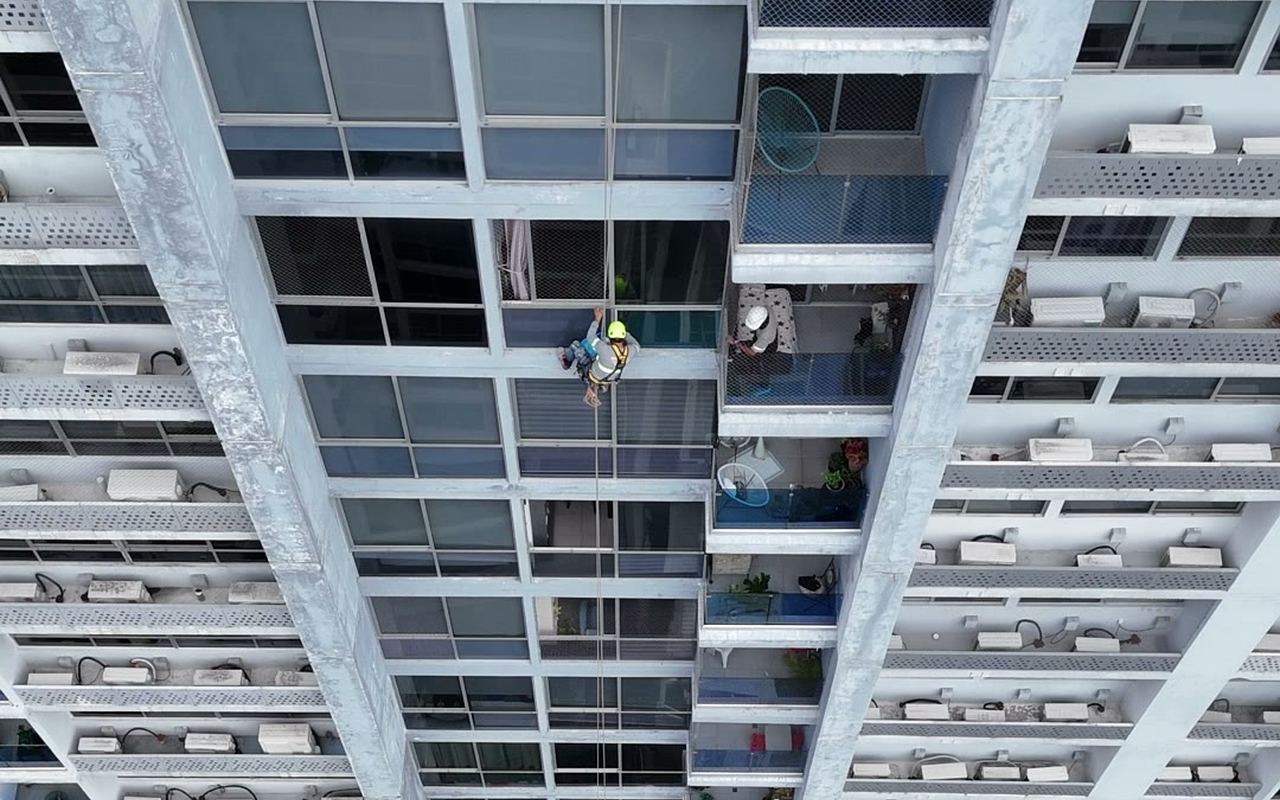 Vista cenital desde dron de un técnico descendiendo por cuerdas entre dos torres de un edificio residencial